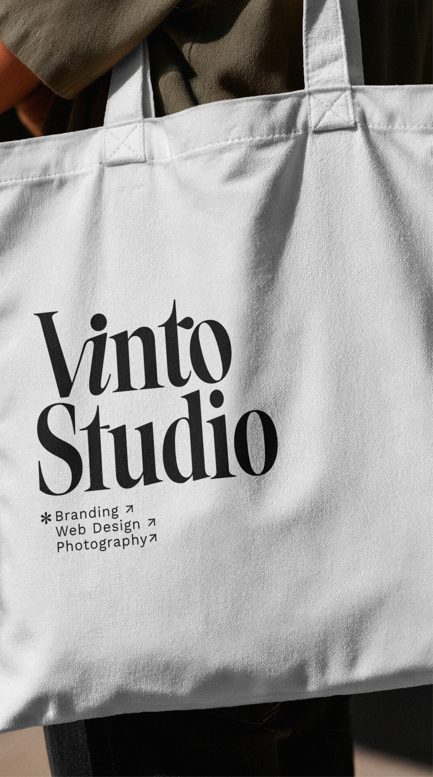 Primer plano vertical de una bolsa de tela blanca con el logotipo minimalista de Vinto Studio impreso en negro.